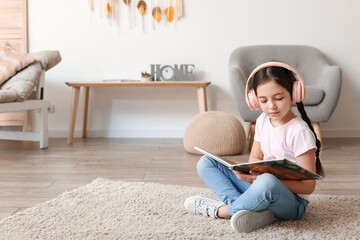 Little girl with headphones reading book at home