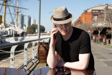 Medium shot of an albino man in a hat talking on his cell phone while sitting in a bar.
