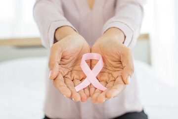 Pink ribbon, on aged hand of illness woman, representing international fabric symbol of breast...