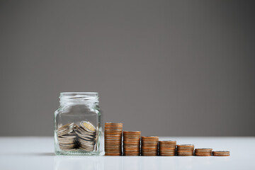 coins into glass jar and stack of coins on gray background. Money management, Personal Financial concept.