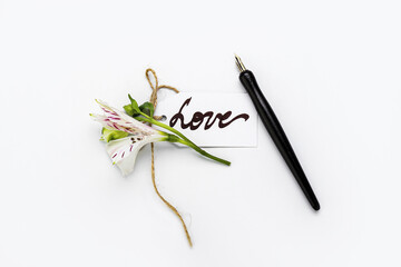Paper with word LOVE, nib pen and flower on white background