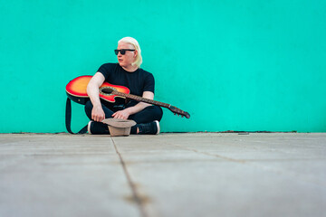 Young albino man with his guitar sitting on the floor resting. Horizontal orientation. Relaxation concept. - Powered by Adobe
