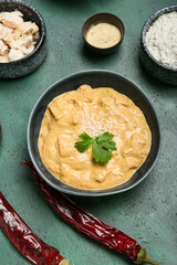 Bowl of tasty chicken curry and ingredients on color background