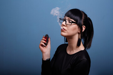 A beautiful girl with dark hair and glasses exquisitely smokes an electronic cigarette