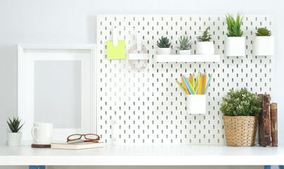 Empty picture frame, coffee cup, books and houseplants on white table.