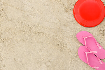 Fototapeta na wymiar Frisbee disk and flip-flops on sand