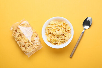 Bowl and bag with tasty cornflakes on color background