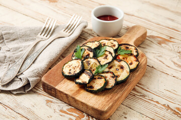 Board with tasty grilled zucchini on light on wooden background