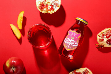Glass and bottle of kombucha tea with fruits on red background