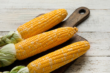 Board with fresh corn cobs on light wooden background