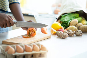 Close up of dark skinned girl hands is preparing fresh salad in kitchen at home, woman cutting tomato