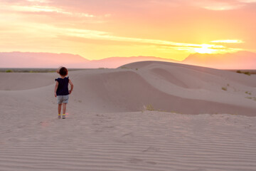Unrecognizable child walking in a desert at sunrise