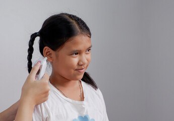 Asian dark-skinned girl smiling awkwardly while doctor measuring her body temperature with digital ear infrared thermometer at clinic