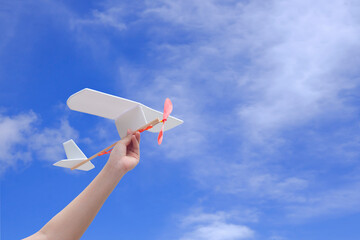 Child hand holding rubber powered aircraft up in the air against blue sky background