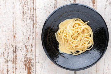 spaghetti carbonara with cream sauce and oregano on top in black ceramic plate on white old wood...