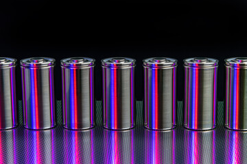 A pack of new modern high-capacity lithium-ion cells. A prototype of new batteries on a steel surface illuminated with red and blue light on a black background