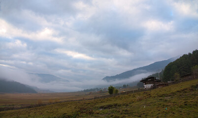 In the evening, the fog surrounds the trees, houses and mountains in the valley. Phobjikha Valley. One of the most lovely and high altitude river valleys, Bhutan. 2019