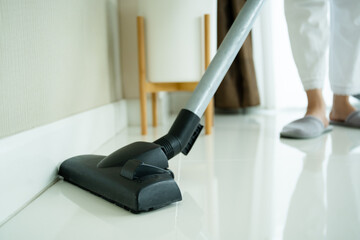 Asian young housekeeper using vacuum machine to clean a dirty floor in the living room close up with copyspace.