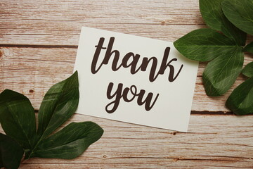 Thank You typography text with green leave decorated on wooden background