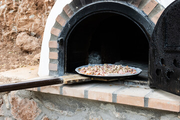 Man putting pizza in handmade white painted wood oven built outdoors with shovel