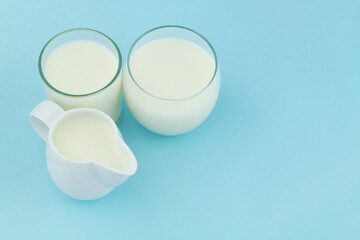 Milk in glasses and white jug on blue background, room for text.