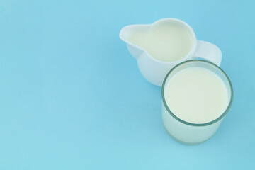 Milk in jug and glass on blue background with copy space for text.