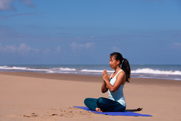 people, fitness, sport and healthy lifestyle concept - young asian woman making yoga pose hands together on tropical beach with blue sky background