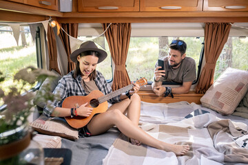 Happy young woman playing guitar on large bed while her husband taking photo or video © pressmaster
