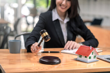 Close-up of woman lawyer holding mallet with model house laptop placed at office.