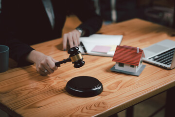 Close-up of woman lawyer holding mallet with model house laptop placed at office.