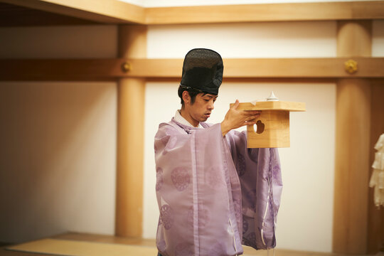 神棚にお供えものをあげる神主