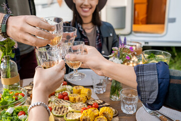 Hands of several friends clinking with glasses of wine by served festive table