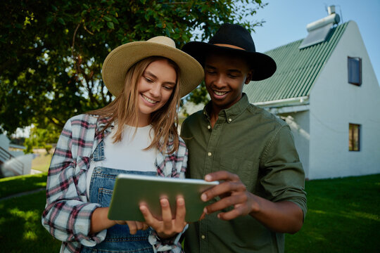 Mixed race male and female farmer standing together by green grass looking at digital tablet 