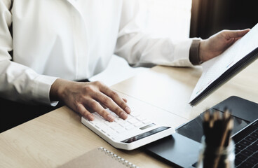 Business woman using calculator to review balance sheet annual using document and laptop computer...