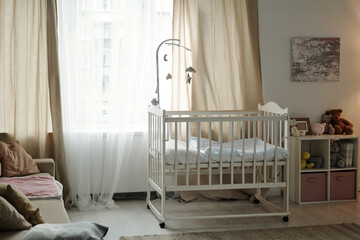 Part of cozy bedroom of newborn baby with crib standing by large window