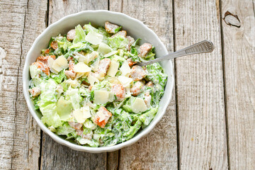 Homemade traditional Caesar Salad with Parmesan Cheese and Croutons in a white bowl on a old white table with leaves and a sauce boat 