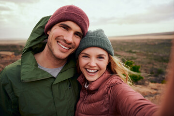 Portrait of cheerful young woman embracing man in winter clothing taking selfie during camping on...