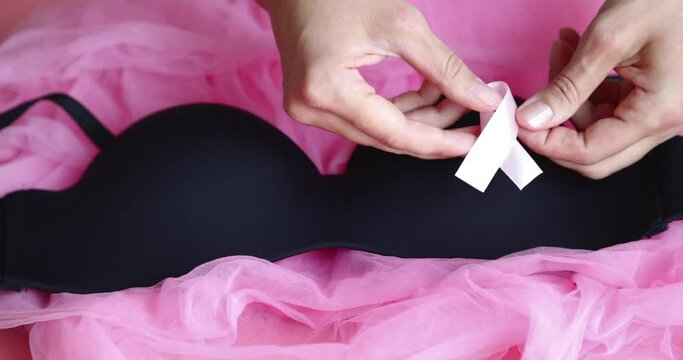 Pink breast cancer awareness ribbon, black underwear and hands on pink background. Slow motion.