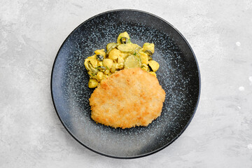 Overhead view of pork schnitzel with potato and pickled cucumber