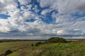 Fototapeta premium Summer field and clouds on the blue sky. A landscape with a bright green field and dramatic clouds against a blue sky.