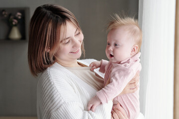 Young smiling female looking at adorable infant on her arms while standing in front of camera