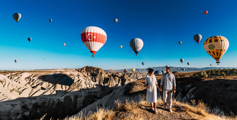 Travel to the tourist places of Turkey. A couple in love stands against the background of balloons in Cappadocia, panorama.Travel to Turkey. Vacation in Turkey. Honeymoon trip. Cappadocia. Copy space - obrazy, fototapety, plakaty