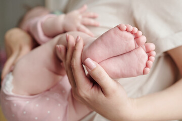 Fototapeta na wymiar Hand of young woman holding bare feet of her cute sleeping baby daughter