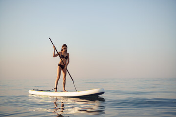 Young attractive woman standing on paddle board