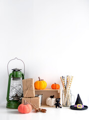 Halloween concept. Festive decor on a white background: a kerosene lantern, knitted pumpkins, cocktail straws, gifts in craft paper. Copy space.