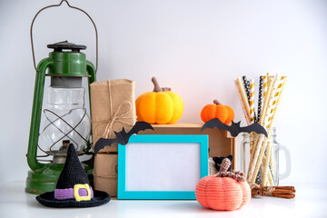 Halloween decor on a white background with a frame with empty space. Knitted pumpkins, witch hat, kerasin lamp, gifts in craft paper, blue frame.