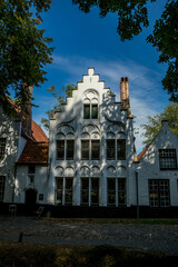 Beautiful white front of a building under the tree shadows, street view of old Bruges, Belgium, cloudy summer day