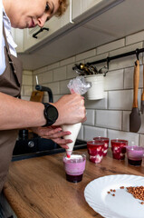 Woman using confectioners bag for putting whipped cream of white color and decorating Birthday cake at home.