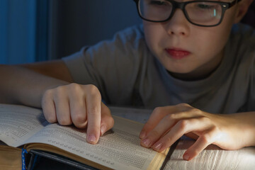 A teenage Caucasian boy with glasses is having a hard time reading a book and trying to make sense...