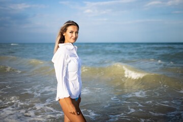 Fototapeta na wymiar Portrait of a girl in a blue swimsuit and white shirt against the background of the blue sea and clear sky